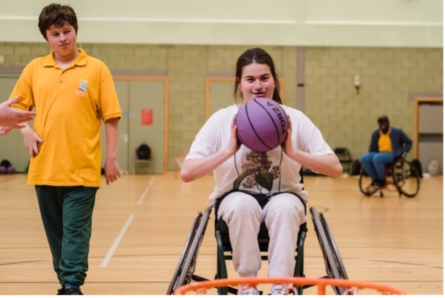 Teenaged girl playing wheelchair basketball. A referee watches her take the shot.